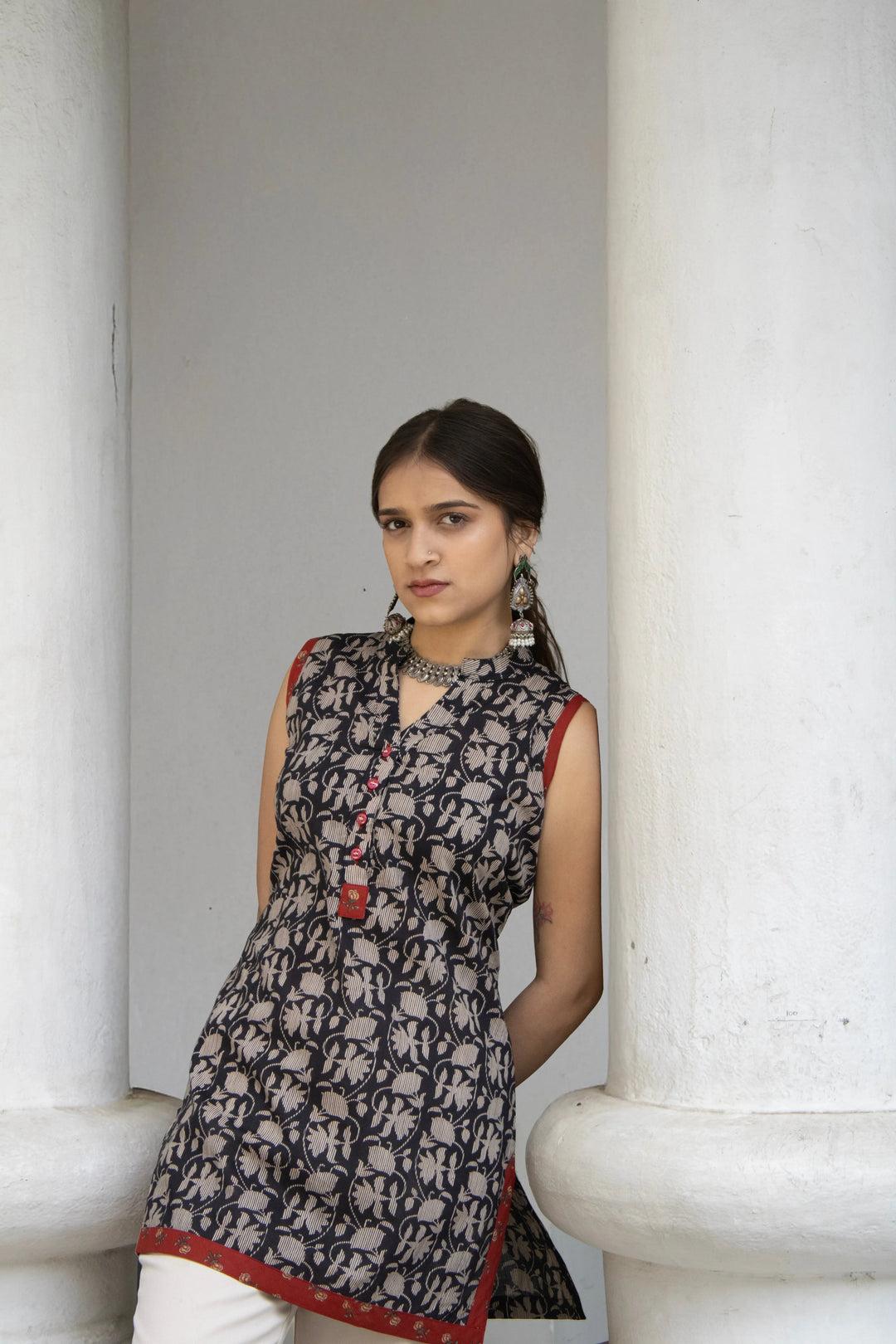 Model wearing a sleeveless black printed short kurti, with red border detailing.