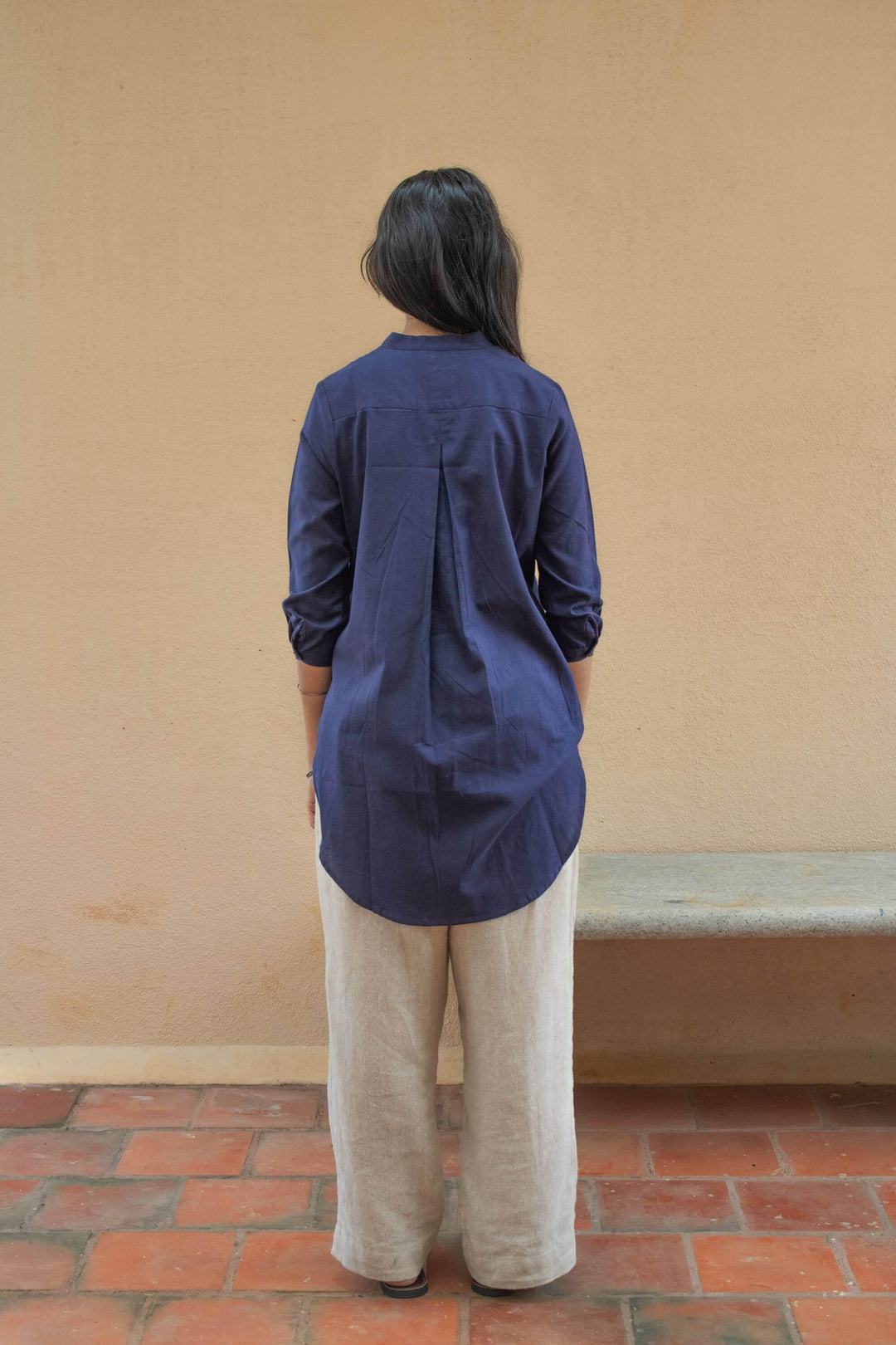 Woman wearing an indigo tunic shirt &amp; light coloured pants. Back View.  