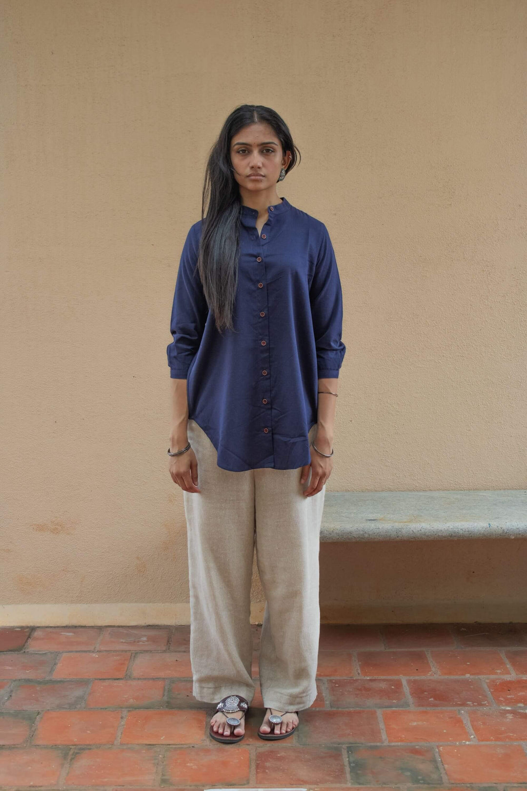 Woman wearing a Indigo Tunic shirt and beige pants standing against a beige wall.