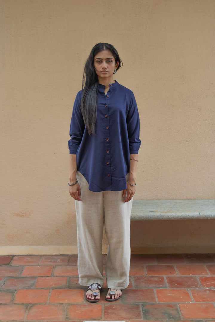 Woman wearing a Indigo Tunic shirt and beige pants standing against a beige wall.